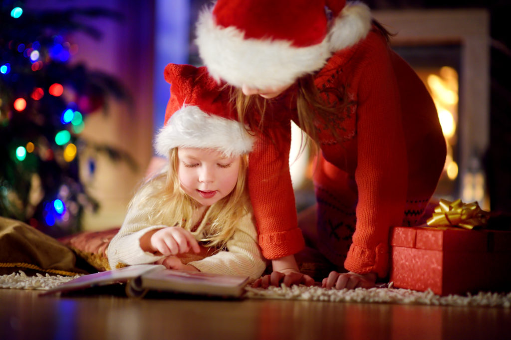 Kinder mit Weihnachtsmützen lesen zusammen in einem Buch