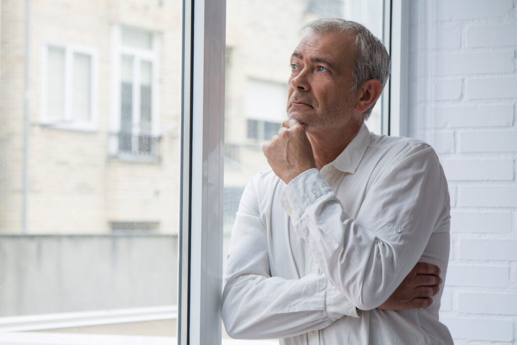 Senior steht am Fenster und denkt nach