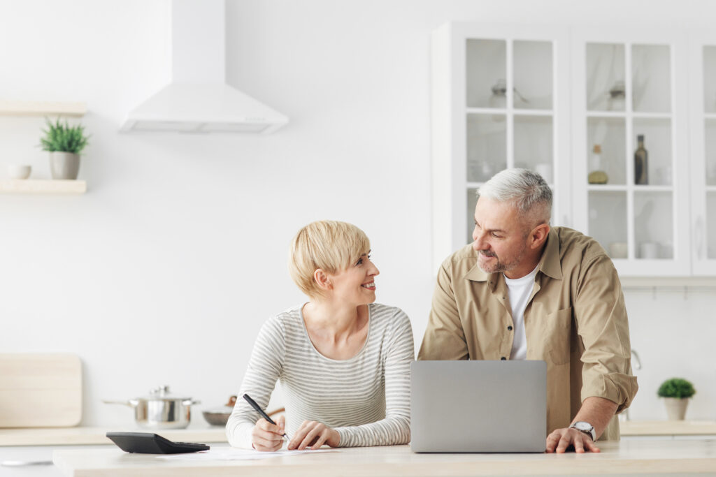 Smiling senior couple spouses use laptop, calculator, new technology paying banking bills online