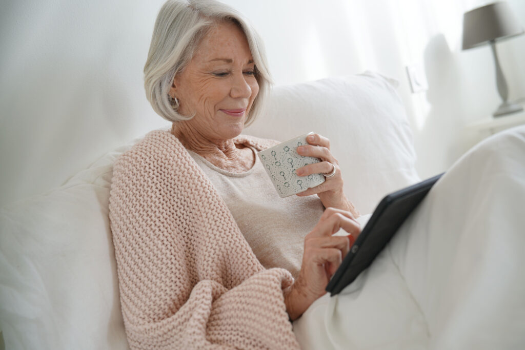 Seniorin sitzt im Bett mit Kaffee und Tablet