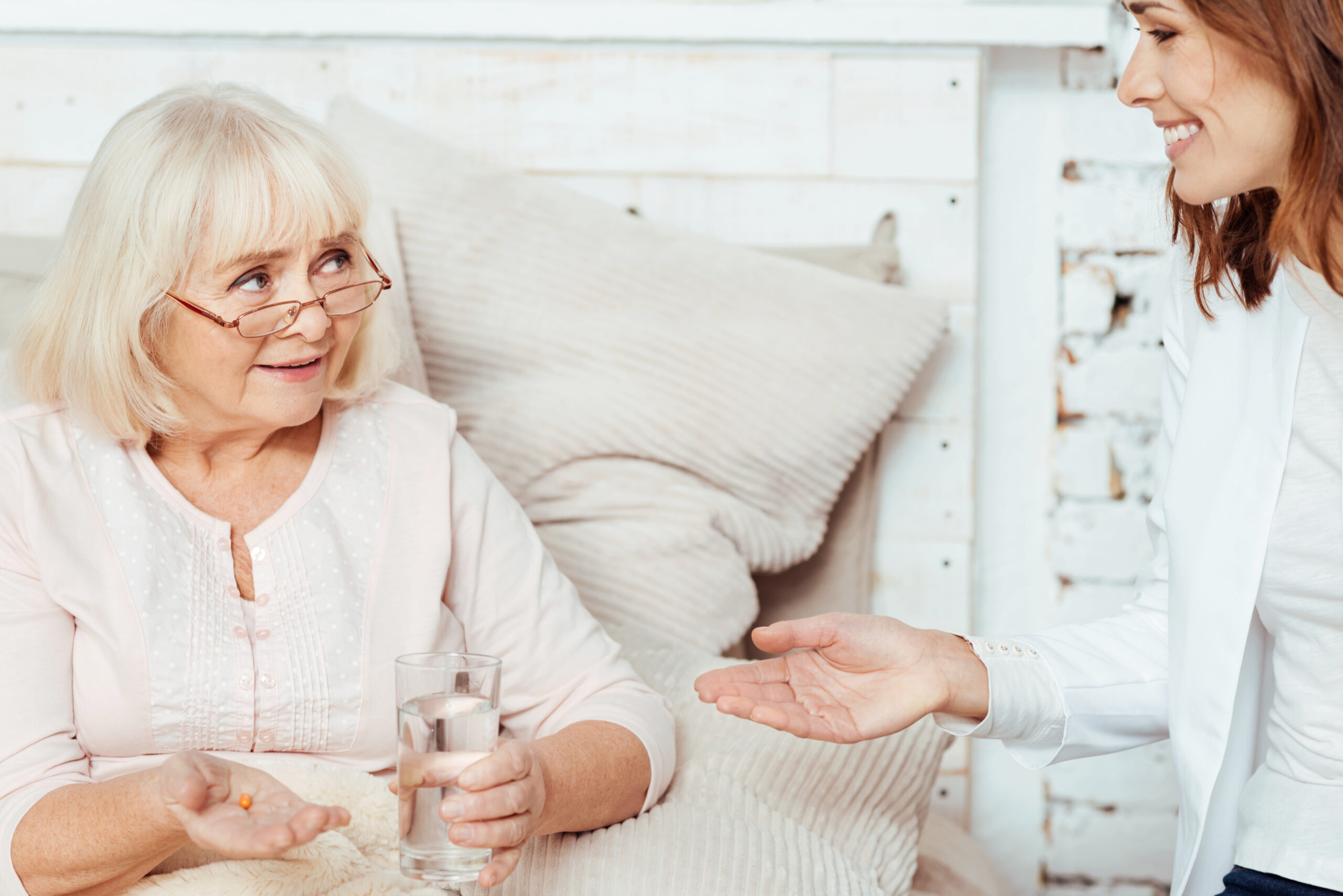 Seniorin sitzt im Bett und bekommt Medikamente von Pflegerin