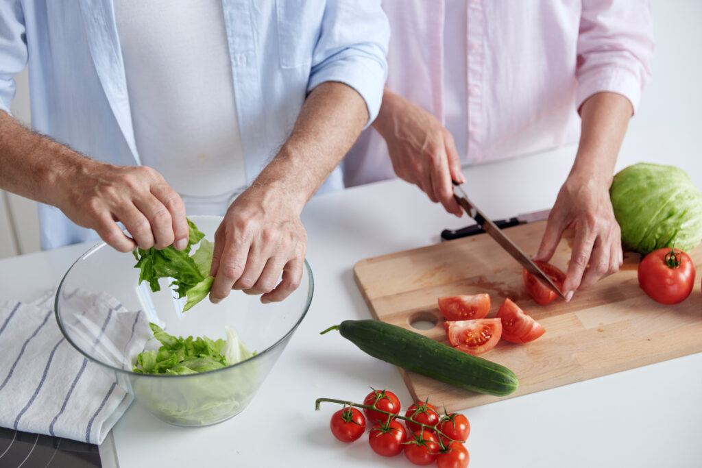 Cropped image of couple cooking salad at kitchen