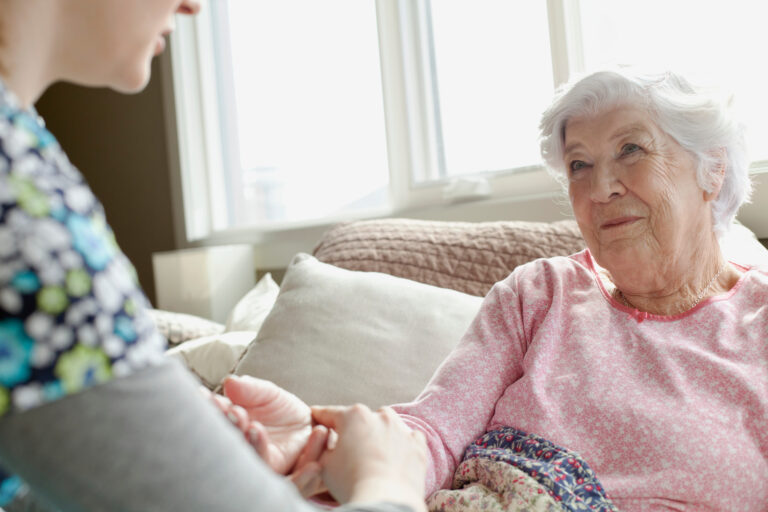 Pflegerin sitzt am Bett einer Seniorin