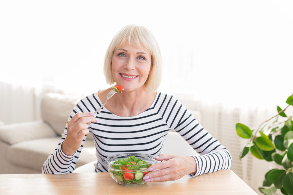 Happy senior lady eating fresh green salad, having rest at home