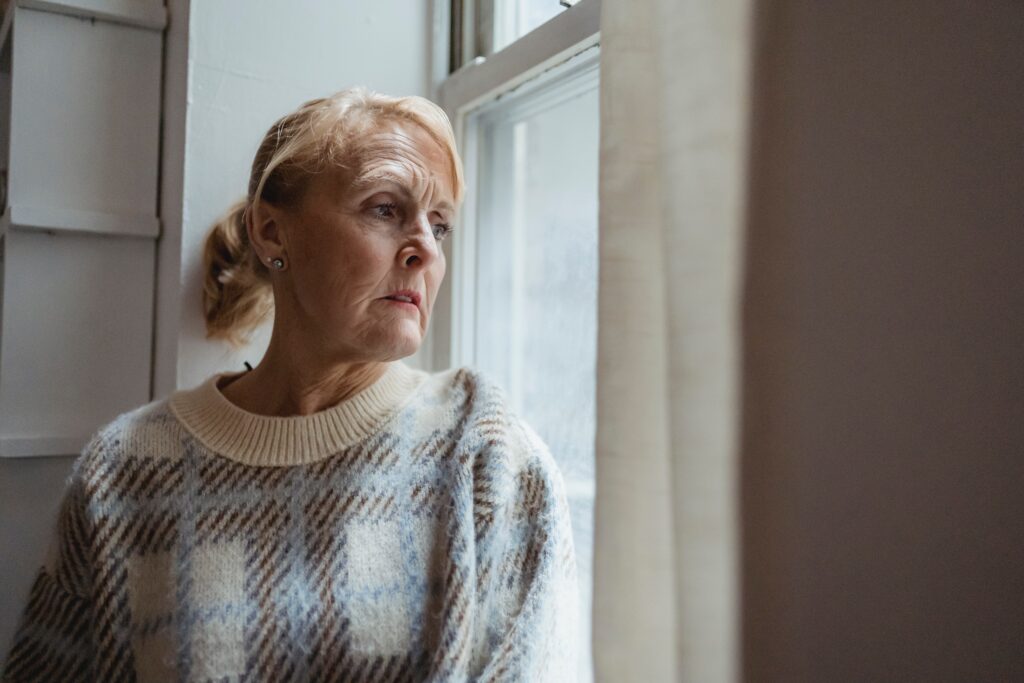 Seniorin am Fenster schaut traurig raus