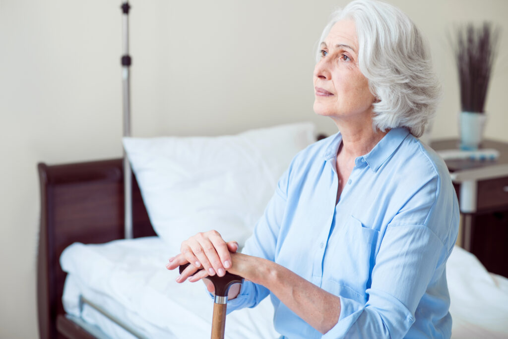 Seniorin mit Gehstock auf dem Bett