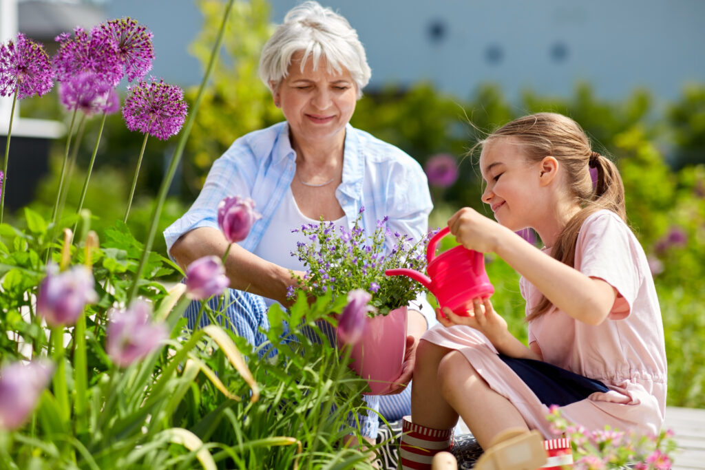 Oma und Enkelin sind im Garten und gießen Blumen